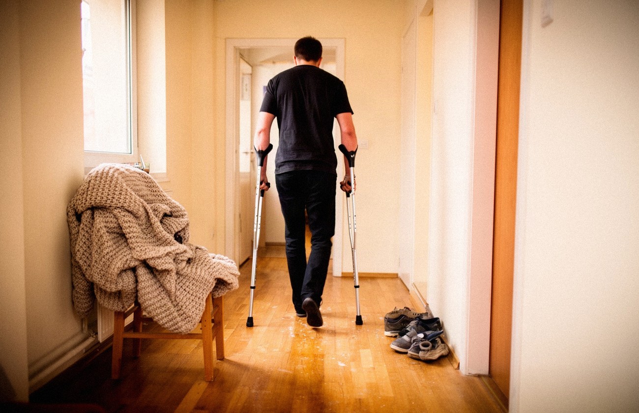 Osoba z kulami łokciowymi idąca korytarzem w domu, widziana od tyłu